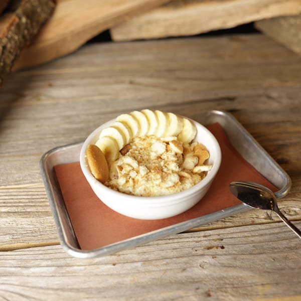 Banana pudding with vanilla wafers and sliced bananas in a white bowl on a metal tray.