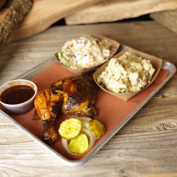 Cedar River BBQ's grilled chicken with potato salad, coleslaw, pickles, onions, and BBQ sauce on a tray.
