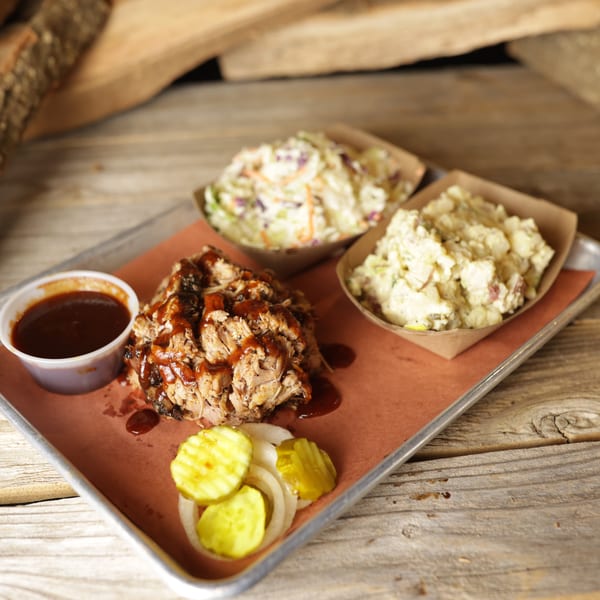 Cedar River BBQ pulled pork with sauce, coleslaw, potato salad, pickles, and onions on a tray.