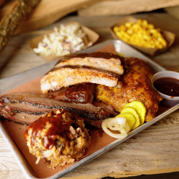 Cedar River BBQ platter with ribs, brisket, pulled pork, pickles, onions, coleslaw, and mac and cheese.
