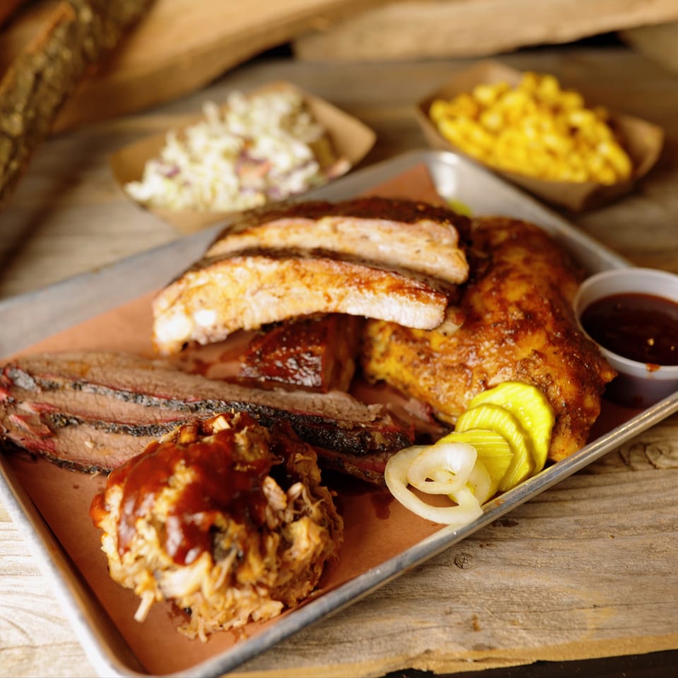 Cedar River BBQ platter with ribs, brisket, pulled pork, pickles, onions, coleslaw, and mac and cheese.