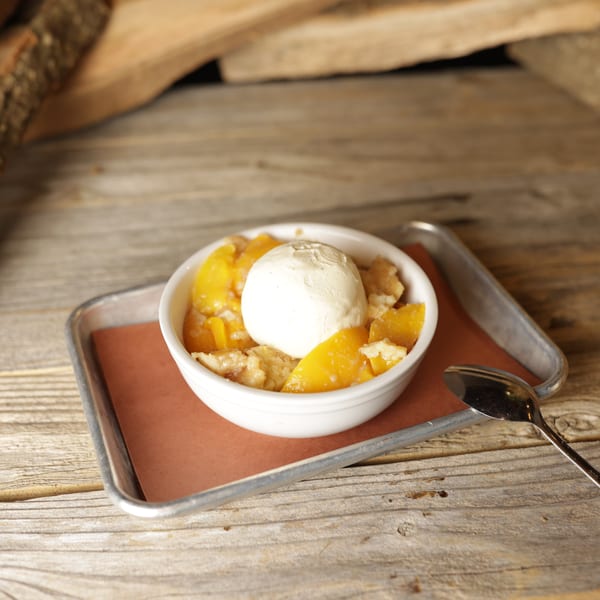 Cedar River BBQ's peach cobbler with a scoop of vanilla ice cream on a metal tray.