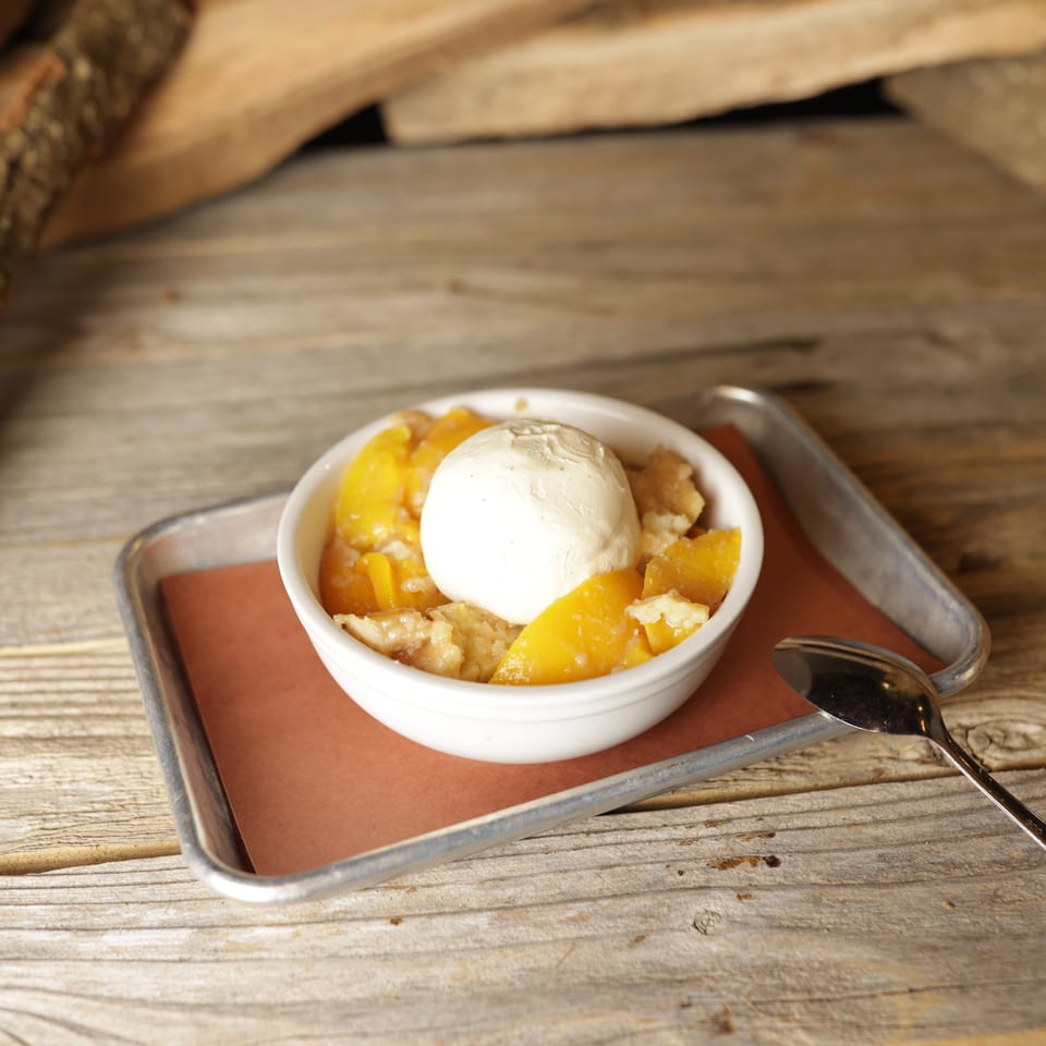 Cedar River BBQ's peach cobbler with a scoop of vanilla ice cream on a metal tray.